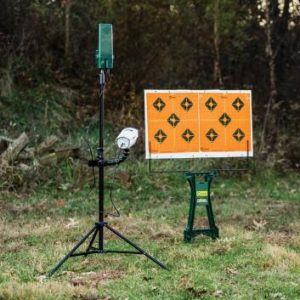 Target practice setup in grassy field, featuring an orange and black bullseye target mounted on a green stand with a green and black tripod nearby, set against a wooded background in Casey, Iowa.