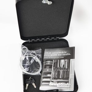 Black portable gun safe case opened, containing a coiled cable lock in transparent packaging, two silver keys with black heads, and a black and white instruction booklet.