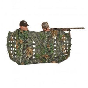 Camo hunting blind with two people concealed, each wearing camouflage hats, aiming firearms through openings.