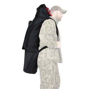 A person wearing camouflage clothing and a cap carries a large black bag with red accents on their back, designed for firearms and ammo.