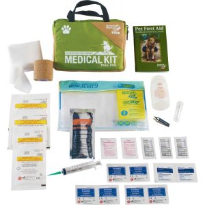 Green and tan medical kit bag with "Medical Kit Trail Dog" text, surrounded by assorted medical supplies including bandages, antiseptic wipes, tweezers, and a pet first aid guide.