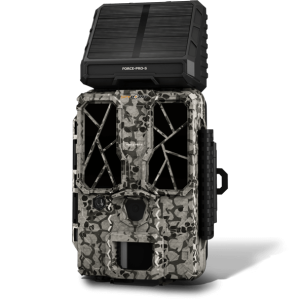A camouflaged trail camera with a black solar panel attached at the top.