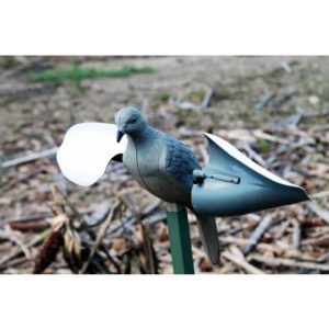 A gray and black bird decoy with white wings perched outdoors on a green pole against a blurred natural background.