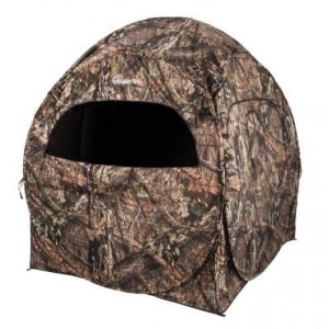 Camouflage tent or hunting blind with green and brown leaf pattern, featuring a large window opening, suitable for outdoor hunting or camping activities.